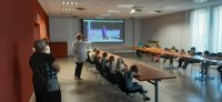 Policjant, opiekunowie i dzieci na sali konferencyjnej w dąbrowskiej komendzie oglądają film edukacyjny