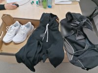 Zdjęcie przedstawia parę butów koloru białego, czarną bluzę, torbę sportowa koloru szaroczarnego.