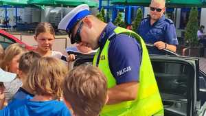 Umundurowany policjant ruchu drogowego rozdający dzieciom odblaski.