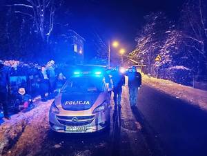 Umundurowani policjanci i społeczność dąbrowska na tle migających na niebiesko sygnałów świetlnych wysyłanych z radiowozów. Oddają hołd poległym policjantom.