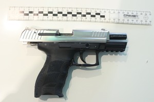 Pistolet koloru srebrno-czarnego, leżący na białym podłożu nad pistoletem linijka do stwierdzenia wielkości broni.