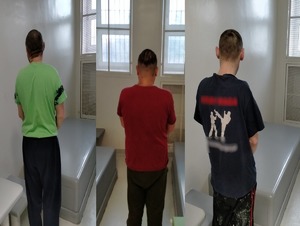 Zdjęcie 3 zatrzymanych mężczyzn stojących tyłem w celi policyjnej.